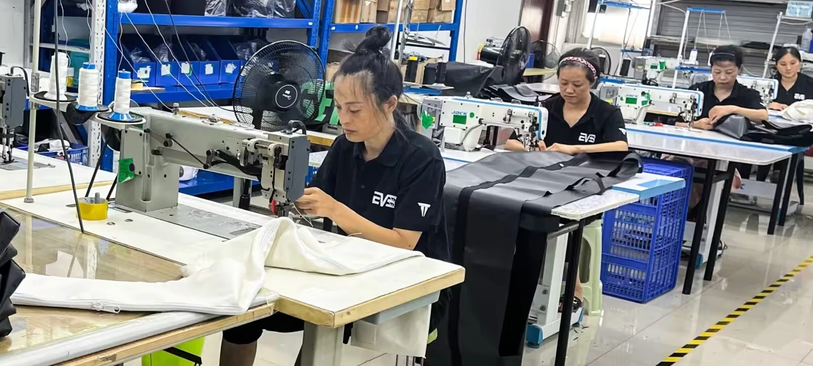 About Our Factory 3 Workers handling fabric at industrial sewing machines in a workshop
