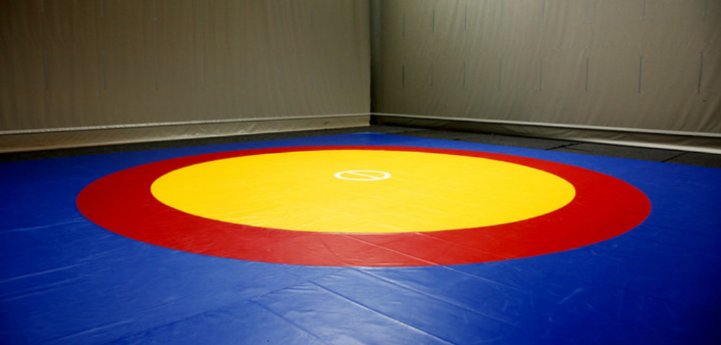 Tapis de lutte installé, avec une zone périphérique bleue, un ring rouge et un centre jaune